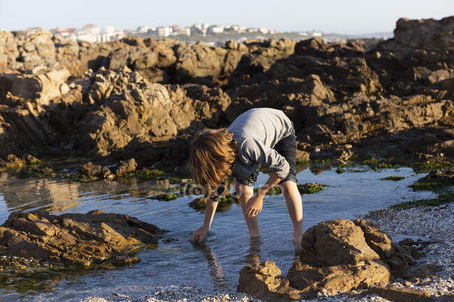 Un chico inclinado a una piscina de rocas, De Kelders, Western Cape, Sudáfrica. - foto de stock