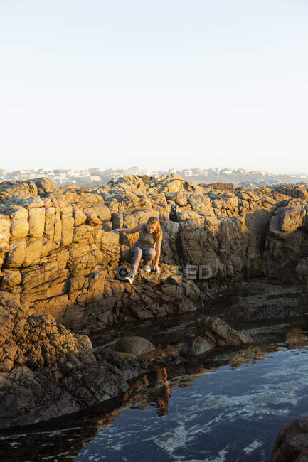 Teenage girl climbing down the jagged rocks on the coastline at De Kelders. — Stock Photo
