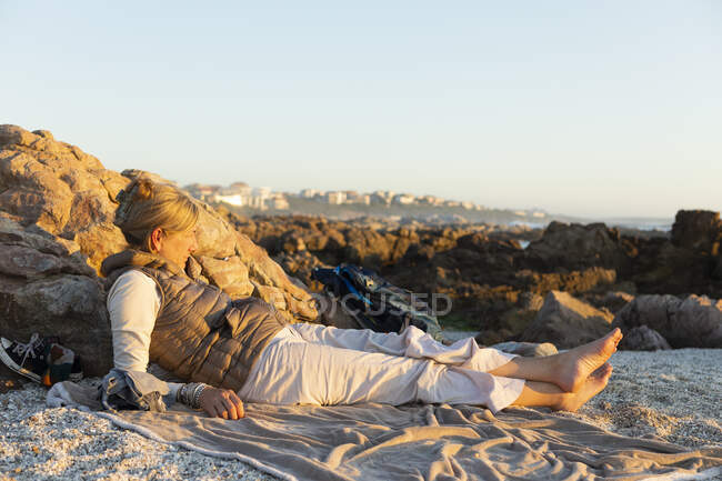 Взрослая женщина, сидящая на песке и отдыхающая на пляже на закате — стоковое фото