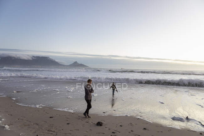 Due persone, un'adolescente e un ragazzo su una spiaggia al tramonto, surfare rotolando in. — Foto stock