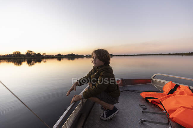 Un joven pescando desde un barco en las tranquilas aguas planas del delta del Okavango al atardecer, Botswana. - foto de stock