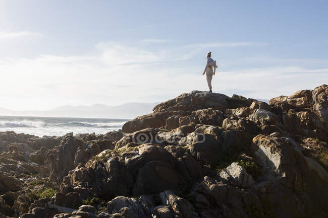 Teenage girl standing on rocky coastline, looking out to sea. — Stock Photo