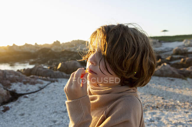 Un garçon sur la plage au coucher du soleil, prenant une collation. — Photo de stock