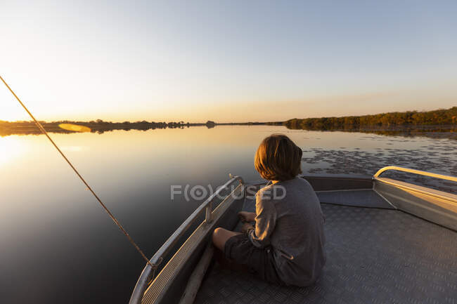 Young boy fishing at the stern of a boat in the Okavango Delta at sunset — Stock Photo