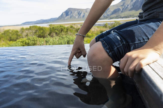 Garçon de huit ans assis au bord d'une piscine d'eau, un fond de montagne — Photo de stock