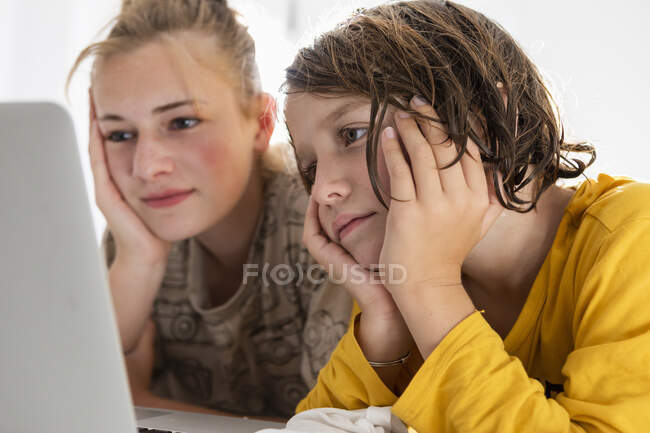 Молодий хлопчик і сестра-підліток діляться ноутбуком, спостерігаючи в спальні. — стокове фото