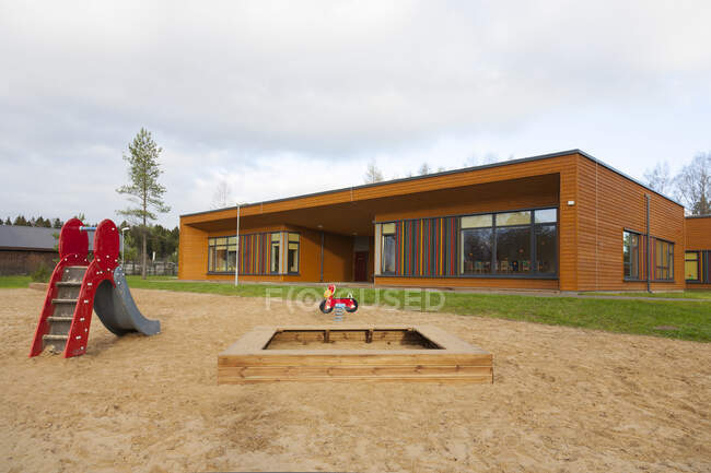Un bâtiment moderne, maternelle ou préscolaire, une grande aire de jeux à fosse de sable avec un toboggan. — Photo de stock