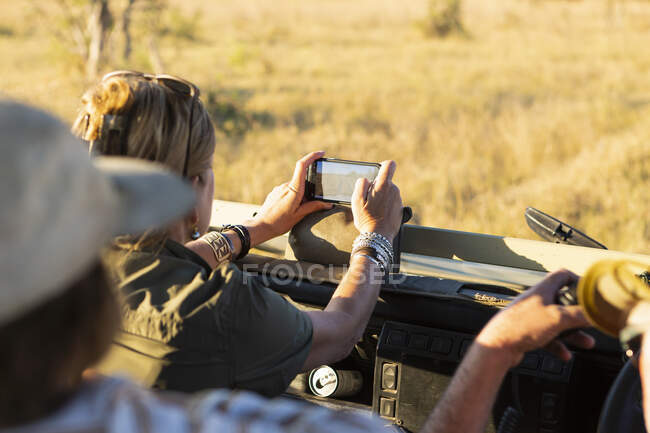 Adult woman taking smart phone image from safari vehicle, Okavango Delta, Botswana. — Stock Photo