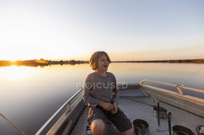 Um menino no convés de um pequeno barco no delta do Okavango ao pôr-do-sol, Botsuana. — Fotografia de Stock