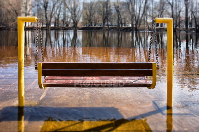 Empty hanging bench swing surrounded by hard frozen ice, riverbank — Stock Photo