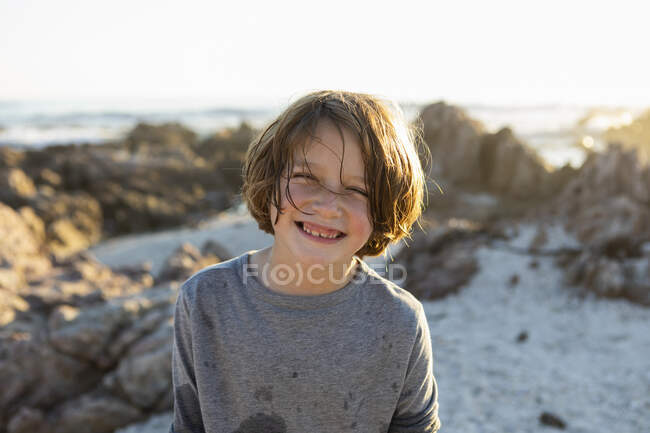 Un jeune garçon souriant sur la plage au coucher du soleil parmi les rochers de De Kelders. — Photo de stock