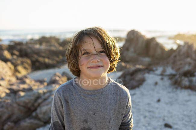 Молодий хлопчик посміхається на пляжі під час заходу сонця серед скель Де Келдерса. — стокове фото