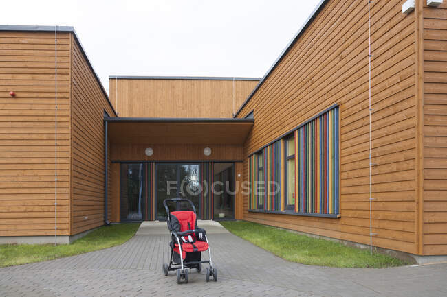 Детская коляска с красным сиденьем возле современного детского сада или дошкольного учреждения — стоковое фото