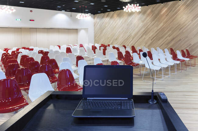 Um computador portátil em um pódio e fileiras de cadeiras em uma sala grande — Fotografia de Stock