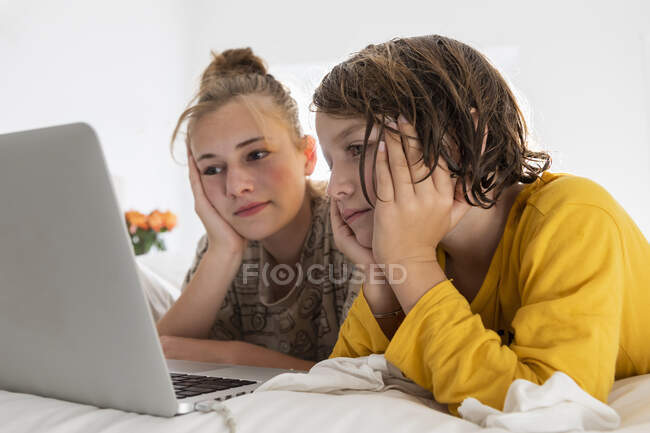 Menino e irmã adolescente compartilhando um laptop, assistindo em um quarto — Fotografia de Stock