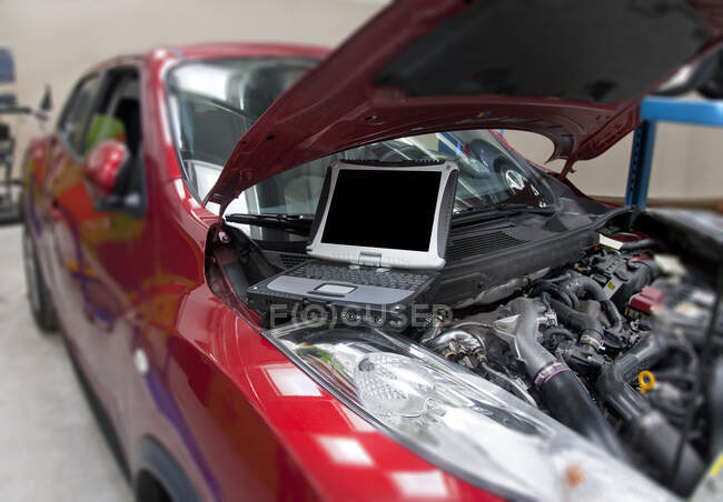 Автомобиль в мастерской и компьютер, выполняющий диагностику двигателя. — стоковое фото