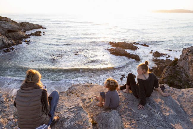 Una famiglia, una madre e due bambini seduti a guardare il tramonto sull'oceano. — Foto stock