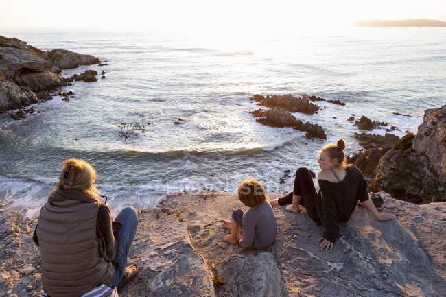 Uma família, mãe e duas crianças sentadas a ver o pôr do sol sobre o oceano. — Fotografia de Stock