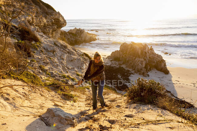 Donna in piedi sulle scogliere sopra una spiaggia agitando un lungo bastone e ridendo — Foto stock