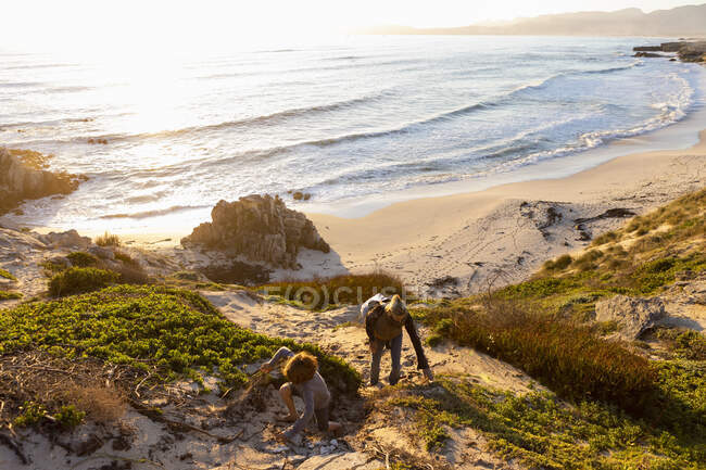 Jovem menino e mulher madura subindo um caminho penhasco ao pôr do sol. — Fotografia de Stock