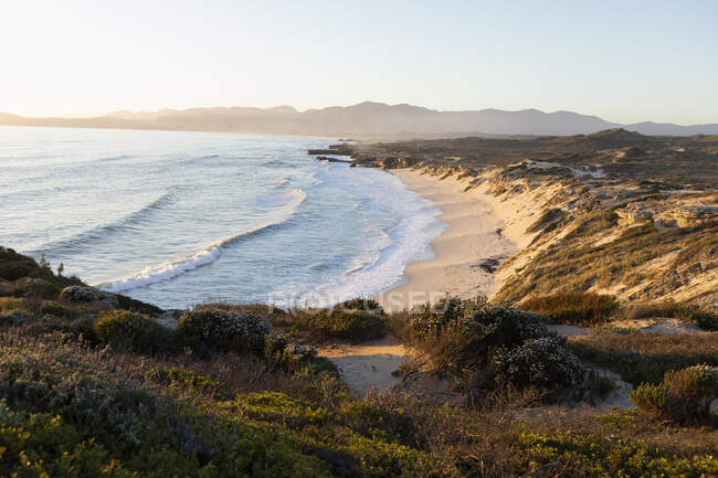 Вид со скал на песчаный пляж и волны, бьющие по берегу. — стоковое фото