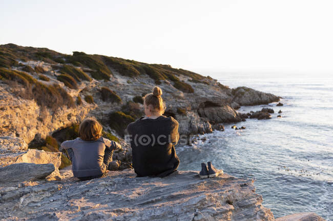 Ragazza adolescente e giovane ragazzo seduto su rocce guardando oltre il mare al tramonto — Foto stock