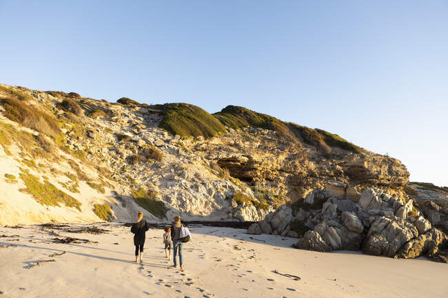 Una famiglia che cammina lungo una spiaggia sabbiosa verso le scogliere. — Foto stock