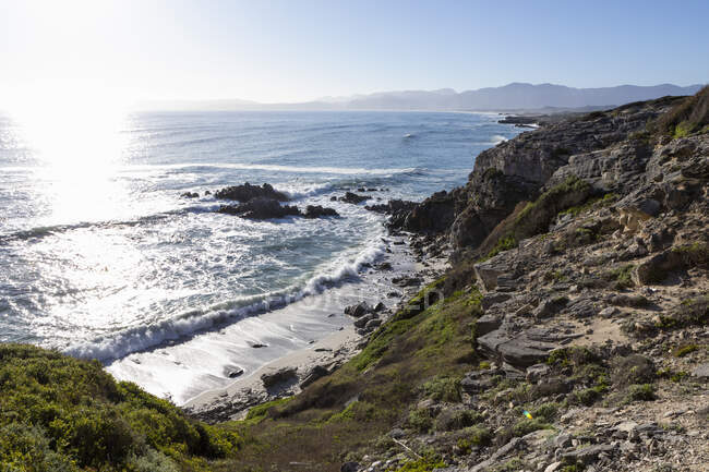 View from the clifftop onto a stretch of beach at high tide, cliffs and dramatic coastline. — Stock Photo