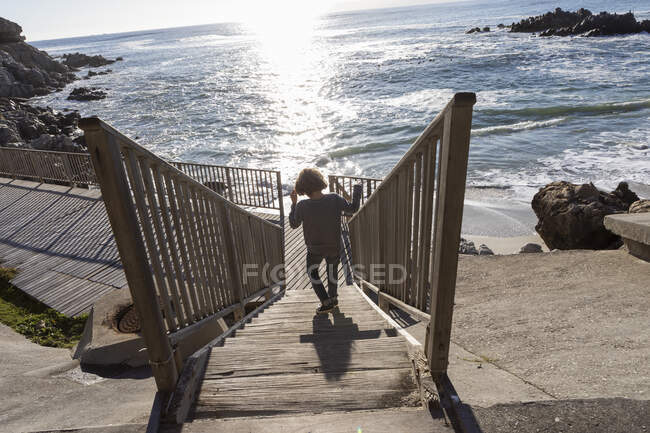 Un chico corriendo hacia la playa por unas escaleras - foto de stock