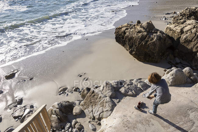 Um rapaz a tirar os sapatos para ir para uma praia de areia — Fotografia de Stock