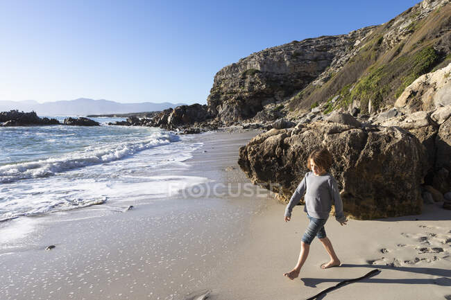 Молодий хлопчик сам на маленькій смузі піску під скелями біля океану.. — стокове фото
