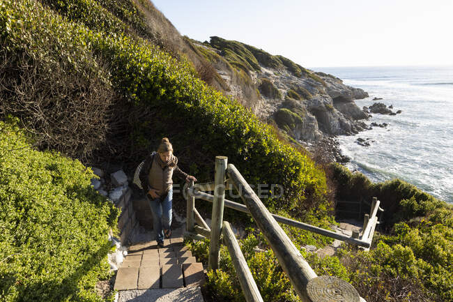 Adult woman walking up steps to the clifftop above a beach. — Stock Photo
