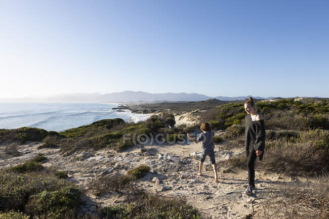 Two children, a teenager and her brother on a sandy path above a beach. — Stock Photo