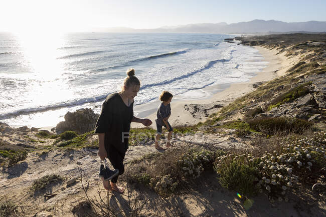 Una adolescente y su hermano corriendo por un camino hacia una playa de arena - foto de stock
