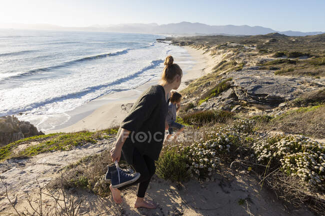 A teenage girl and her brother running down a path towards a sandy beach — Stock Photo