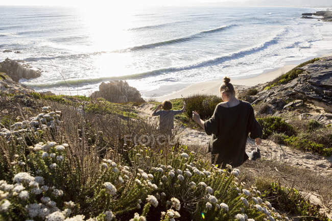 A teenage girl and her brother running down a path towards a sandy beach — Stock Photo