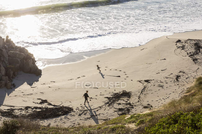 Двое детей бегают и оставляют следы на мягком песке пляжа — стоковое фото