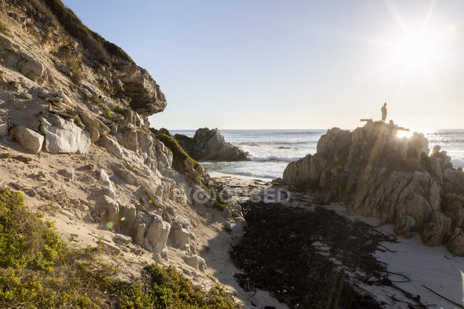 Девочка-подросток балансирует на неровной скале на песчаном пляже — стоковое фото