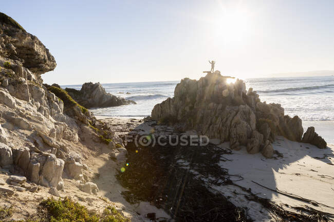Мальчик, стоящий на вершине скалы высоко над песчаным пляжем — стоковое фото