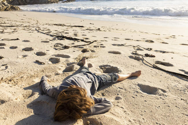 Jeune garçon assis sur une plage de sable — Photo de stock
