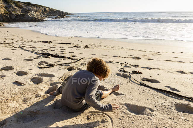 Молодий хлопчик сидить на піщаному пляжі — стокове фото