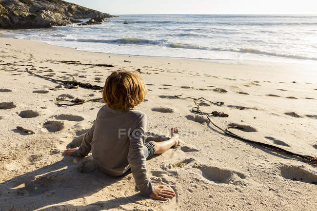 Молодий хлопчик сидить на піщаному пляжі — стокове фото