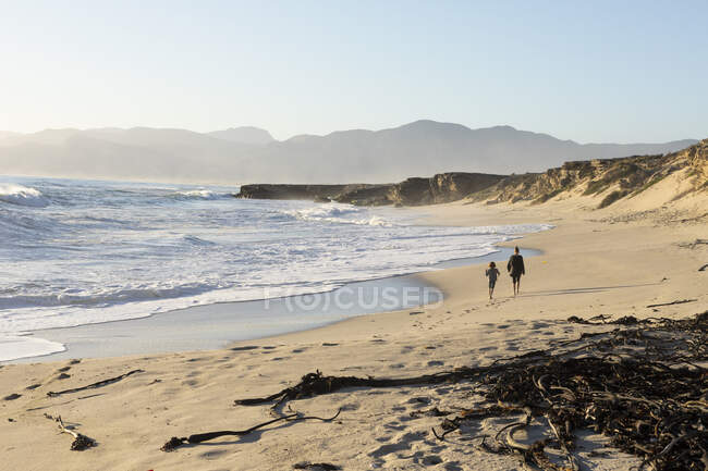 Deux personnes marchant le long d'une plage de sable, un adolescent et un garçon — Photo de stock