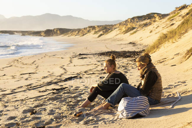 Zwei Personen, Mutter und Tochter sitzen auf dem Sand und blicken aufs Meer — Stockfoto