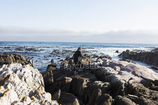 Дівчинка-підліток, що йде через зубчасті скелі, досліджує кам'яні басейни біля океану — стокове фото