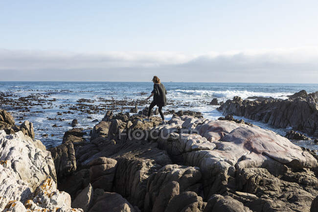 Teenage girl walking across jagged rocks, exploring rock pools by the ocean — Stock Photo