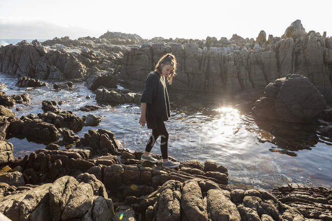 Девочка-подросток ходит по зазубренным скалам, исследует скальные бассейны у океана — стоковое фото