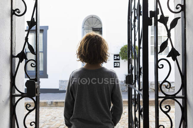 Un chico de pie mirando por las puertas abiertas de hierro. - foto de stock
