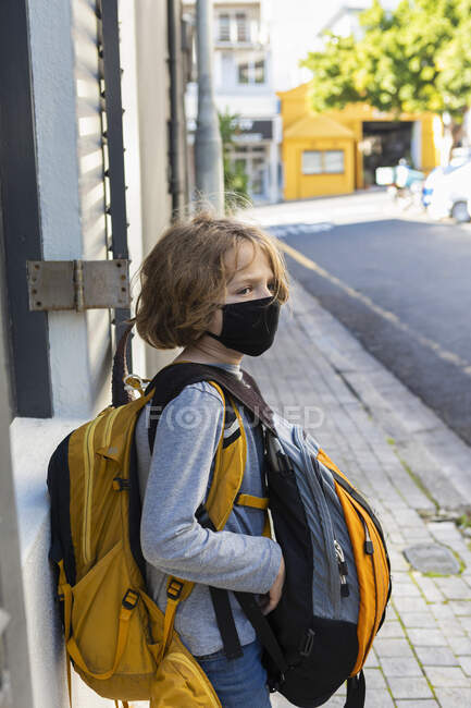 Un garçon portant un sac à dos avec un masque noir dans une rue. — Photo de stock