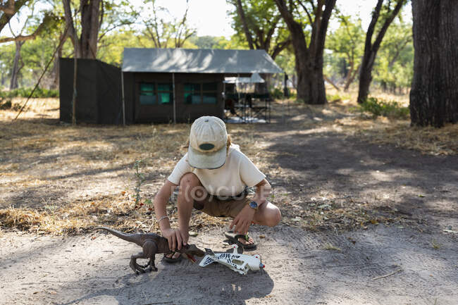 Giovane ragazzo in tenda campo safari giocare con un dinosauro giocattolo e un aeroplano giocattolo. — Foto stock